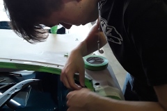 An apprentice practices masking a panel to get it ready for paint